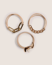 Three gold hair ties with different designs on a beige background