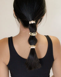 Person with a ponytail using gold hair ties against a neutral background