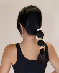 Person with a ponytail wearing gold hair ties against a plain background