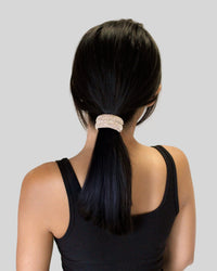 Person with a high ponytail wearing a rhinestone cuff pony in black top against a plain background