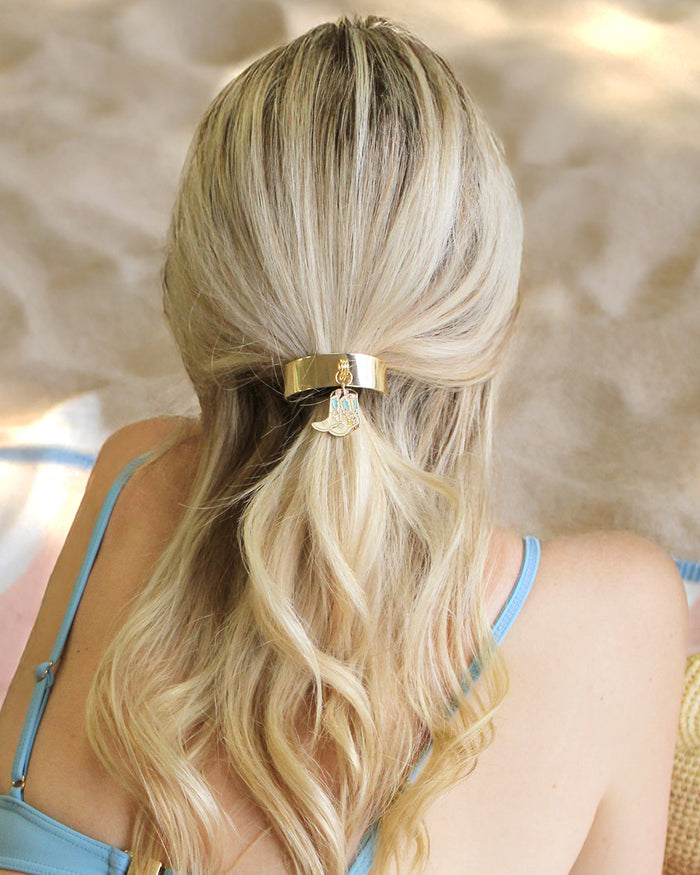 Person with blonde hair tied back with a gold hair tie against a blurred background