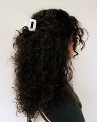 Person with curly hair wearing a white hair clip against a plain background