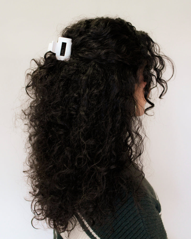 Person with curly hair wearing a white hair clip against a plain background